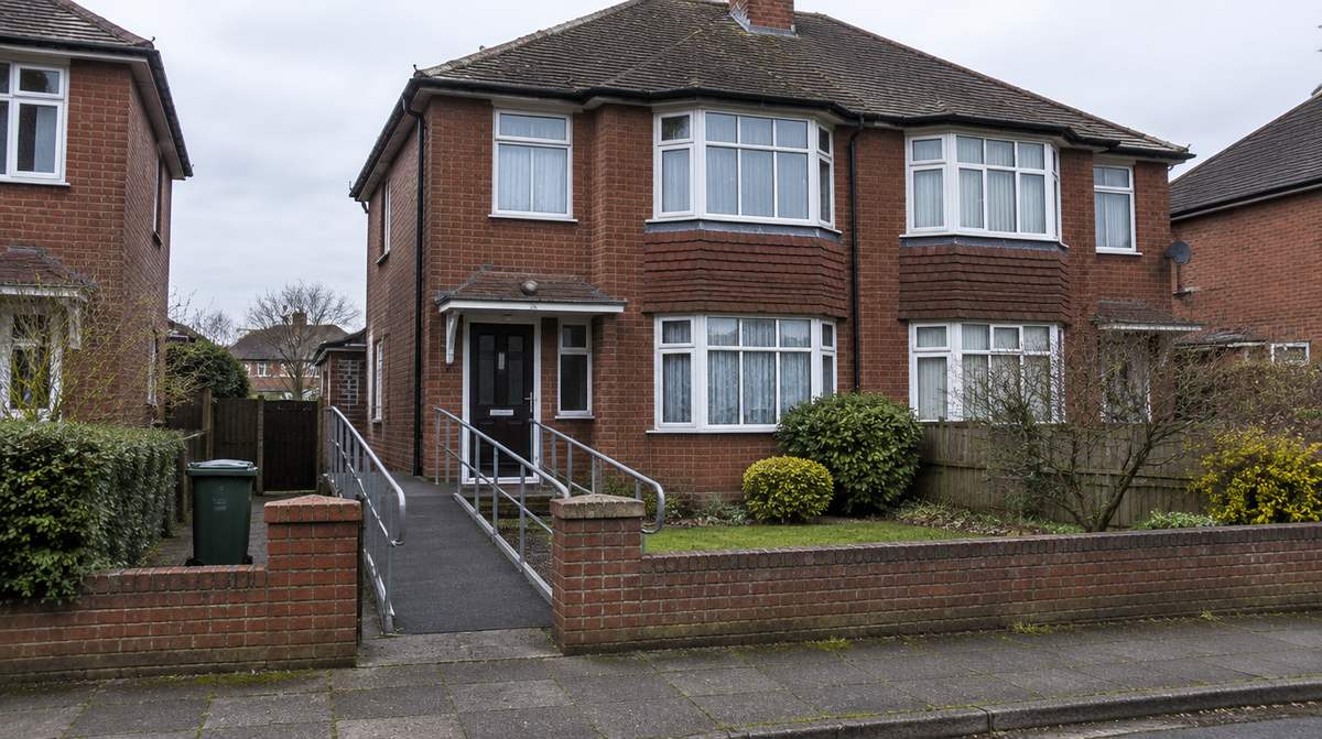 An ordinary red-brick semi-detached house with a ramp to the front door, used as a supported living home